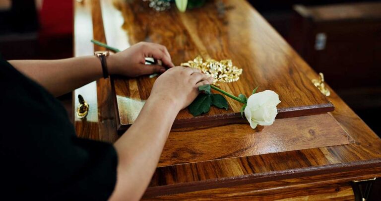 Friends and family gathered around a memory table with personal photos, candles, and flowers at a memorial service.